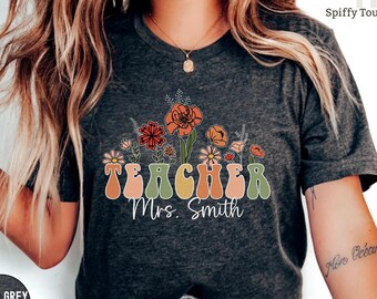 Pode incluir: Camiseta de cor cinza escuro heather com um design floral retrô e o texto "TEACHER Mrs. Smith".