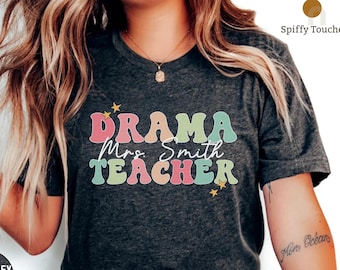 Puede incluir: Una camiseta de color gris oscuro jaspeado con el texto "DRAMA Mrs. Smith TEACHER" en letras retro de colores con estrellas.