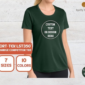 May include: A forest green short-sleeved crew neck t-shirt featuring a white circular graphic on the chest with the text CUSTOM TEXT OR DESIGN HERE. The shirt is identified as a Sport-Tek LST350 Posicharge Competitor Tee, available in 7 sizes.