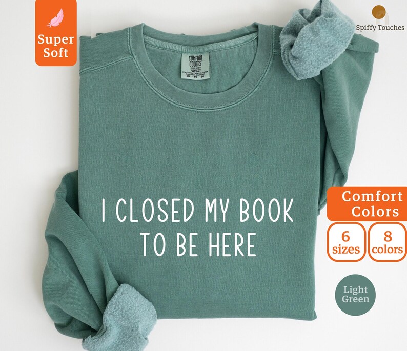 May include: A light green sweatshirt with the text "I closed my book to be here" printed in white. The sweatshirt is available in 6 sizes and 8 colors.