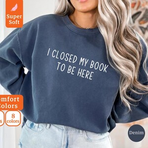May include: A dark blue sweatshirt with the text "I closed my book to be here" in white. The sweatshirt is made of a soft, comfortable material.