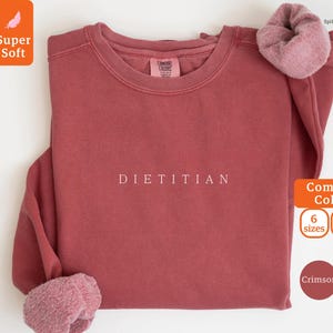May include: Crimson red sweatshirt with the word "DIETITIAN" printed in white on the front. The sweatshirt is made of a soft, comfortable fabric and is available in sizes 6 and 8.