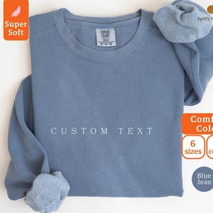 May include: A blue jean sweatshirt with the text "CUSTOM TEXT" printed on the front. The sweatshirt is available in 6 sizes and 8 colors.
