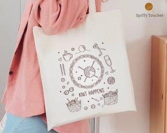 May include: Cream-colored tote bag with a black illustration of knitting-related items. The design includes a ball of yarn, knitting needles, scissors, and the text "KNIT HAPPENS". The bag is held by a person wearing a pink jacket.