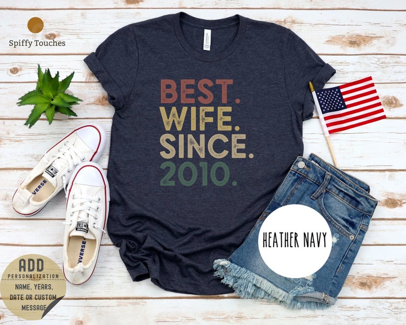 Puede incluir: Una camiseta azul marino jaspeada con el texto "BEST. WIFE. SINCE. 2010." en una fuente de estilo vintage. El texto est&aacute; en tonos de rojo, naranja, amarillo y verde.