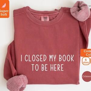 May include: Crimson red sweatshirt with the text "I CLOSED MY BOOK TO BE HERE" in white. The sweatshirt is available in 6 sizes and 8 colors.