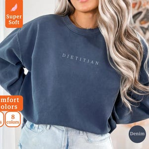 May include: A dark blue sweatshirt with the word "DIETITIAN" printed in white on the front. The sweatshirt is made of a soft, comfortable fabric and has a relaxed fit.