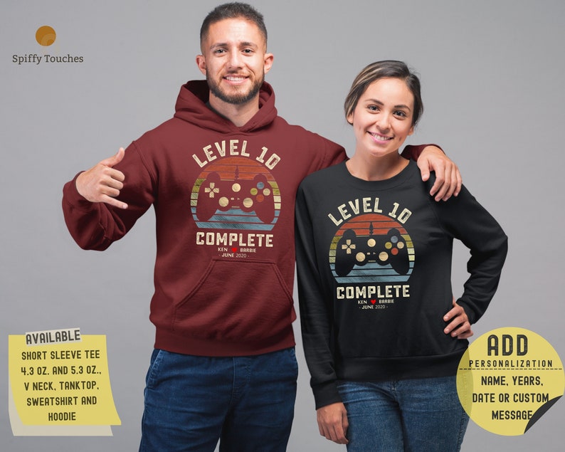 May include: A burgundy hoodie and a black long-sleeve shirt with a retro video game controller design. The text on the shirts reads "Level 10 Complete" with the name "Kin" and the date "June 2020". The shirts are available in various styles.