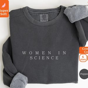 Peut inclure: Un sweat-shirt gris foncé avec le texte "WOMEN IN SCIENCE" imprimé en blanc. Le sweat-shirt est fait d'un matériau doux et confortable et est disponible en 6 tailles et 8 couleurs.
