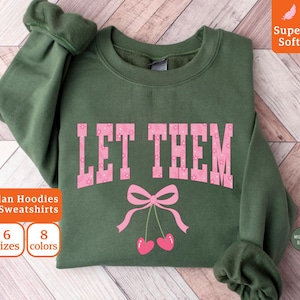 Könnte beinhalten: Militärgrünes Sweatshirt mit dem pinkfarbenen Schriftzug "LET THEM", verziert mit einer rosa Schleife und Kirschen. Das Sweatshirt ist als "Super Soft" gekennzeichnet und in 6 Größen und 8 Farben erhältlich.