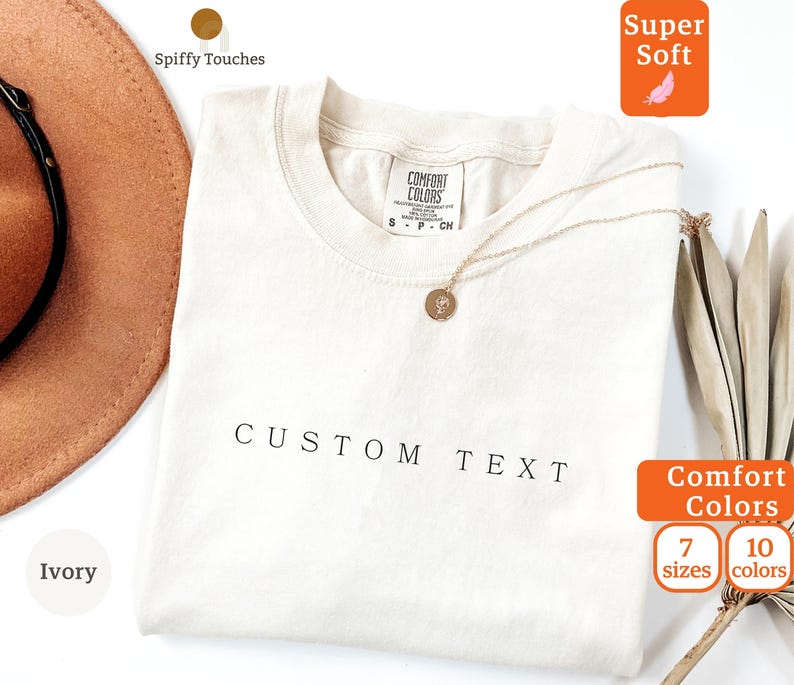 以下が含まれることがあります： アイボリー色のTシャツで、前面に「CUSTOM TEXT」の文字がプリントされています。このTシャツは柔らかく快適な生地で作られており、7サイズと10色からお選びいただけます。