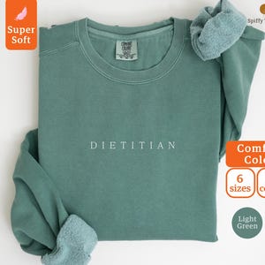 May include: A light green sweatshirt with the word "DIETITIAN" printed in white on the front. The sweatshirt is made of a soft, comfortable fabric and is available in 6 sizes and 8 colors.