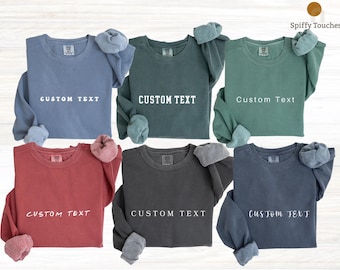 Puede incluir: Seis sudaderas de cuello redondo en azul, verde oscuro, verde salvia, rojo, gris carbón y azul marino. Cada prenda presenta el texto CUSTOM TEXT impreso en blanco en el pecho. Las sudaderas tienen mangas largas y cuello redondo.