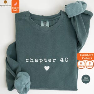 May include: Blue spruce-colored sweatshirt with the text "chapter 40" and a white heart. The sweatshirt has long sleeves and a crew neck. The image also shows the words "Comfort Colors", "6 sizes", and "8 colors".