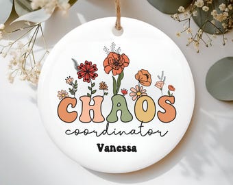 May include: White ceramic ornament with the words "CHAOS coordinator" in a retro font, with floral accents. The name "Vanessa" is below the text. A decorative item for the home.
