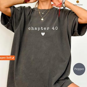 May include: Dark grey t-shirt with the text "chapter 40" and a white heart. The shirt has a relaxed fit and is made of a soft material. The shirt is a solid color and has short sleeves.