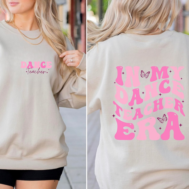 May include: A light beige sweatshirt with the text "Dance Teacher" in pink letters on the front and "In My Dance Teacher Era" in pink letters on the back. The back design also includes two pink butterflies.