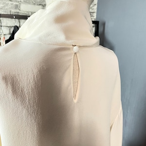 May include: A white silk blouse with a keyhole back detail and a single button closure.