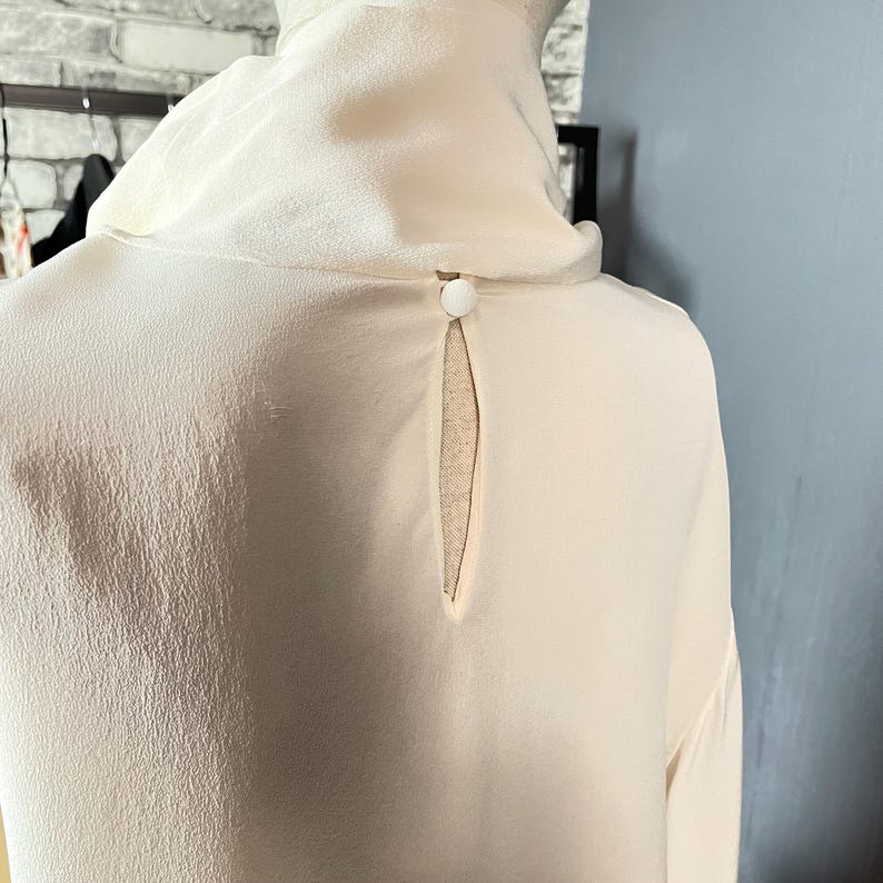 May include: A white silk blouse with a keyhole back detail and a single button closure.