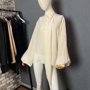 May include: A white, long-sleeved blouse with a high neck and a tie at the front. The blouse has a loose, flowing fit and is made of a lightweight fabric.