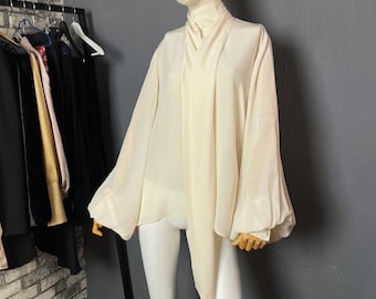 May include: A white, long-sleeved blouse with a high neck and a tie at the front. The blouse has a loose, flowing fit and is made of a lightweight fabric.