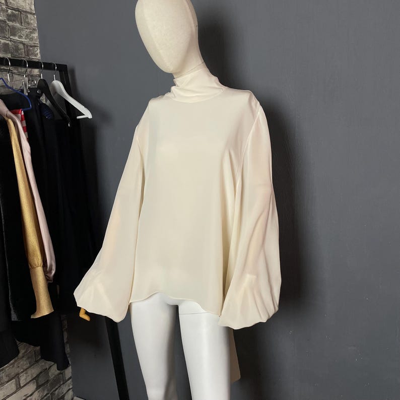 May include: A white, long-sleeved blouse with a high neck and balloon sleeves.