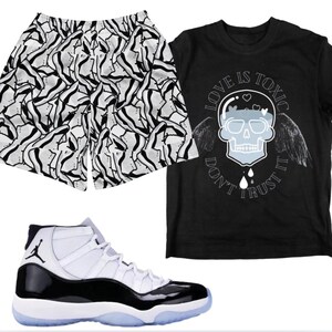 Puede incluir: Una camiseta negra con un gráfico de calavera y el texto "LOVE IS TOXIC DON'T TRUST IT". También se muestran pantalones cortos deportivos blancos y negros con un patrón ondulado y zapatillas altas blancas y negras con suela translúcida.