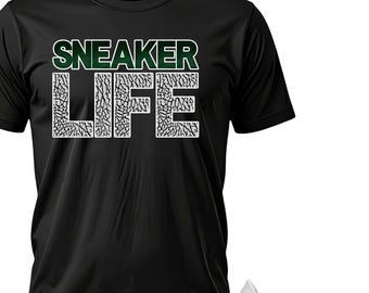 May include: Black t-shirt with the text "SNEAKER LIFE" in white and green. The word "LIFE" has a gray elephant print pattern. A white and green sneaker with gray accents is next to the shirt.