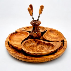May include: A round wooden serving tray with four individual bowls and a central holder for four small skewers. The tray and bowls are made of light brown olive wood.