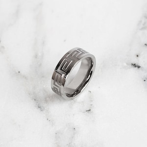 May include: A silver ring with a geometric pattern engraved around the band.