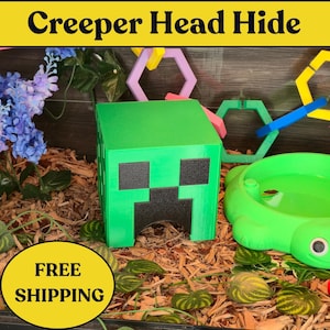 May include: A green, cube-shaped hideaway for a reptile, designed to resemble a Minecraft Creeper head. The hide features black square details for eyes and mouth. The image also includes a green water dish and the text "Creeper Head Hide".