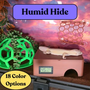 May include: A reptile terrarium setup featuring a brown humid hide with a digital display showing temperature and humidity. A gecko rests on top. Other accessories include a green geometric hide and a honeycomb-shaped climbing structure. Text reads "Humid Hide" and "18 Color Options."