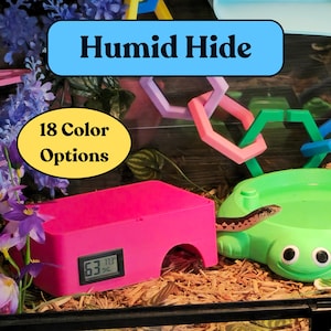 May include: A pink Humid Hide with a digital display showing humidity and temperature, next to a green water dish. The image also shows a snake and the text "18 Color Options" and "Humid Hide".