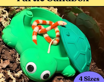 Puede incluir: Un arenero verde brillante con forma de tortuga, tapa de caparazón extraíble y dos grandes ojos móviles en la cabeza. Una pequeña serpiente a rayas naranjas, blancas y amarillas descansa en el interior. Texto: Turtle Sandbox, 4 Sizes, 5 Colors.