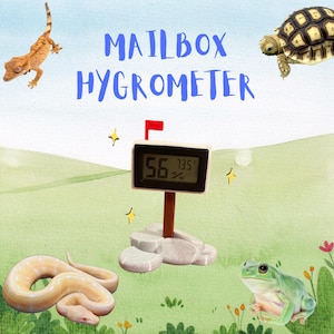 May include: A white mailbox-shaped digital hygrometer with a red flag on top. The display shows 56% humidity and 73.5 degrees. The hygrometer is sitting on a gray rock with a green background.