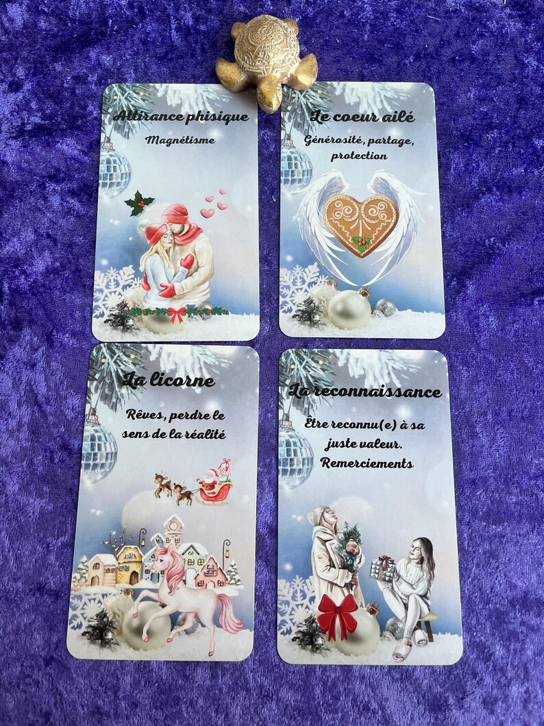 May include: Four tarot cards with French text and illustrations. The cards feature images of a couple, a heart with wings, a unicorn, and two women. A gold turtle figurine sits above the cards.