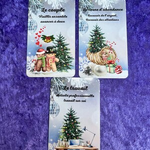 May include: Three tarot cards with winter-themed illustrations. The cards feature images of Christmas trees, ornaments, and text in French. A golden turtle figurine sits above the cards on a purple surface.