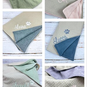 Op de afbeelding: Vijf verschillende honden dekens met gepersonaliseerde namen. Elke deken is beige met een poot afdruk en een geborduurde naam. De dekens zijn gemaakt van een zacht, pluche materiaal en perfect om te knuffelen met je harige vriend.
