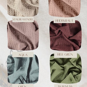 Op de afbeelding: Waffle-stofstalen in verschillende kleuren, waaronder beige, roze, bruin, groen en grijs. De stalen zijn gelabeld met Duitse namen: Kitt, Staubrosa, Staublevandel, Heidekraut, Aqua, Hell Gr&uuml;n, Gr&uuml;n en Walnuss.