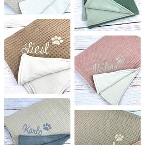 Op de afbeelding: Zes verschillende hondenbedden met gepersonaliseerde namen geborduurd erop. De bedden zijn gemaakt van een zacht, pluche materiaal en zijn verkrijgbaar in verschillende kleuren, waaronder beige, bruin, groen, roze en grijs. Elk bed heeft een pootprintontwerp.