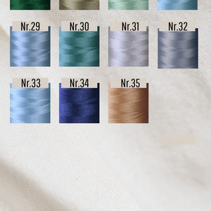 Op de afbeelding: Een garenkleurenkaart met het Duitse woord "Garnfarben" bovenaan. De kleuren zijn genummerd van 25 tot 35. De kleuren omvatten groen, bruin, lichtblauw, donkerblauw en beige.