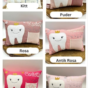 May include: A selection of tooth fairy pillows in different colours, each with a smiling tooth design, a small pocket, and a name embroidered on the pillow. The pillows are in shades of pink, cream, and white, with gold crown accents.