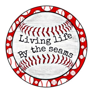 May include: A white wooden circle with a red border and a baseball graphic. The graphic has red stitching and white baseballs around the border. The text "Living life By the seams" is printed in black on the circle.