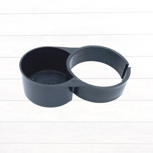 May include: Black plastic cup holder with a circular opening and a larger, open ring on the side.