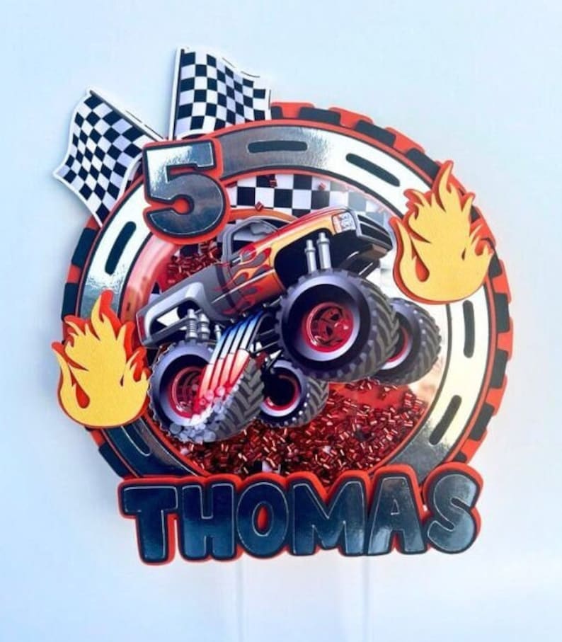 May include: A red, black, and silver monster truck cake topper with a checkered flag, flames, and the number 5. The name "Thomas" is written in black letters below the truck.