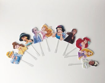 May include: A set of ten princess character cake toppers. The toppers are printed on cardstock and feature various Disney princesses, including Cinderella, Snow White, Ariel, and Belle. The toppers are attached to clear plastic sticks.