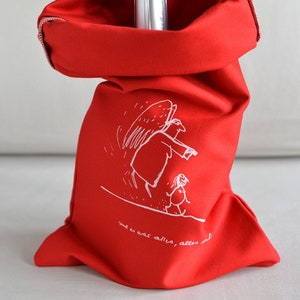 May include: A red fabric gift bag with a white illustration of an angel and a child. The bag is filled with a silver bottle of champagne. The text on the bag reads "und es war alles, alles gut".