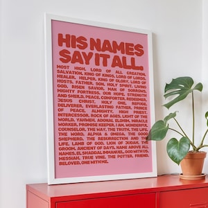 May include: A red metal cabinet with two doors and a framed print that reads "HIS NAMES SAY IT ALL" in red text. A potted plant and a woven magazine rack are next to the cabinet.