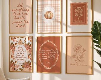 May include: Six framed art prints with gold frames are displayed on a wall. The prints feature inspirational quotes, floral designs, and a pumpkin illustration. The color palette includes warm tones of peach, brown, and cream, creating a cozy aesthetic.