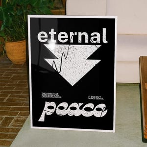 May include: A framed black and white art print with the word "eternal" at the top. Below is a white arrow design with a textured effect, and the word "peace" at the bottom. The print also includes the phrases "THE KIND THAT UNDERSTANDING" and "IT DOESN'T MAKE SENSE."